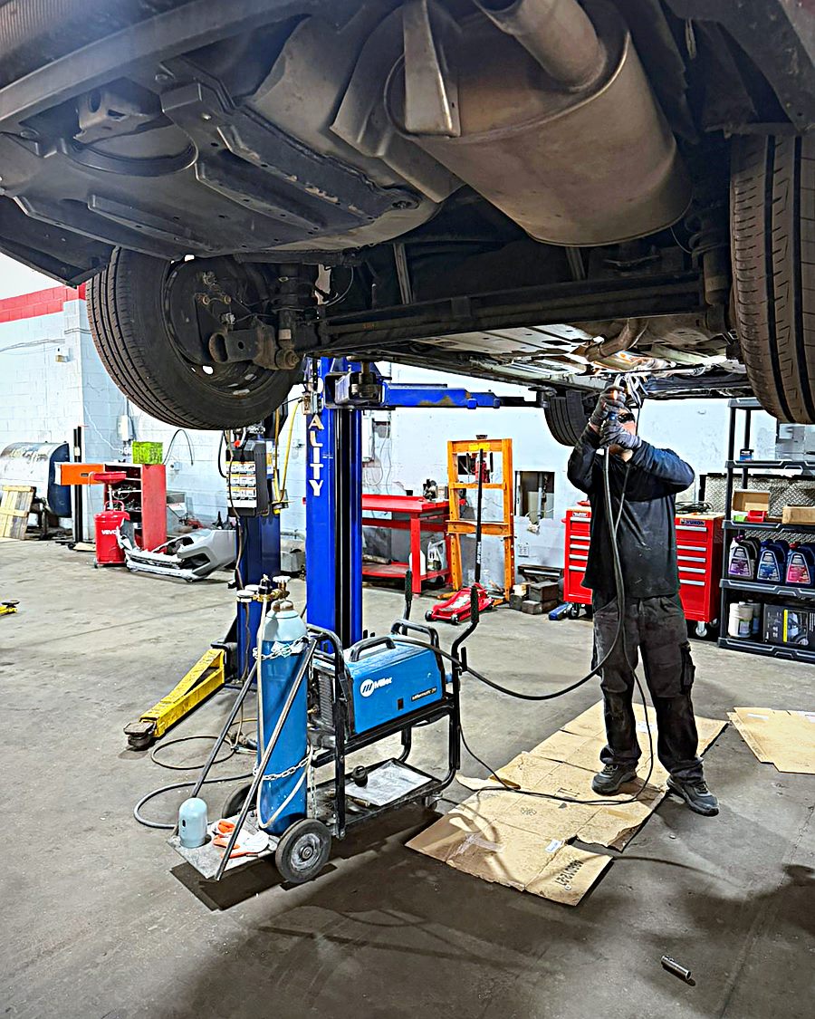 Technician welding under a car raised on a lift in the Unique shop